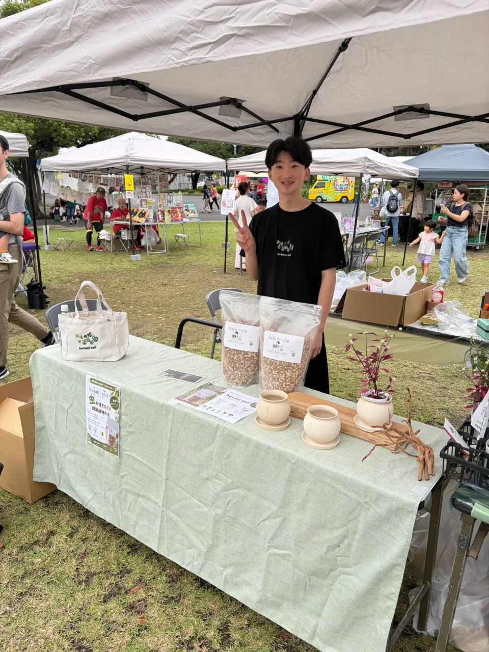 botani soilの袋、鉢、植物がテーブルに並び、スタッフが立つ出展ブース
