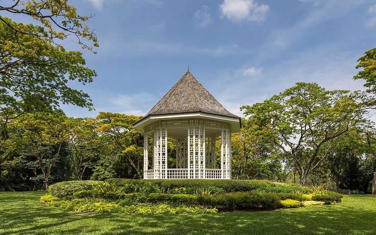 Large trees and lawn surround the white Bandstand at Singapore Botanic Gardens
