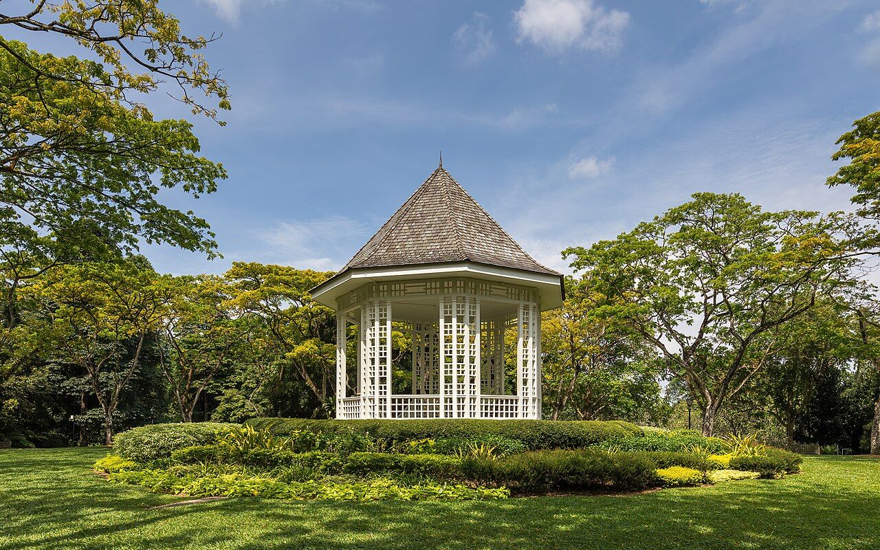 Large trees and lawn surround the white Bandstand at Singapore Botanic Gardens